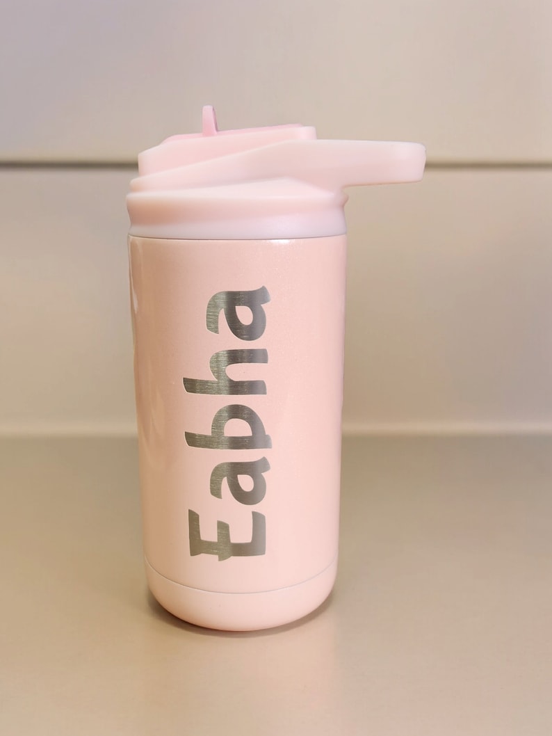 Puede incluir: Una botella de agua de acero inoxidable rosa con tapa de pajita. La botella tiene el nombre "Eabha" grabado en el lateral.