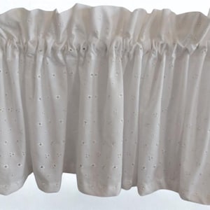 May include: White eyelet fabric valance with a ruffled top edge. The fabric is gathered at the top and has small, evenly spaced cut-out details. The bottom edge has a slight scalloped shape.