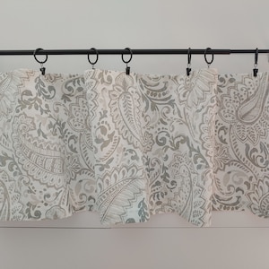 Peut inclure: Une cantonnière blanche à motif paisley gris est suspendue à une tringle à rideaux noire. La cantonnière est en tissu léger et présente un design simple et élégant.