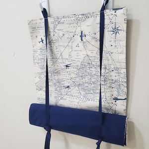 May include: A cream-colored canvas map of the world with blue airplane illustrations and a compass rose. The map is rolled up and hanging from two white hooks with blue ribbon ties.