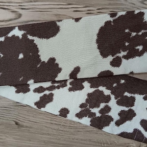May include: A brown and white cow print fabric with a smooth texture.