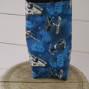 May include: A blue fabric tote bag with a Star Wars theme. The bag features a space scene with starships and the words "Star Wars" repeated throughout.