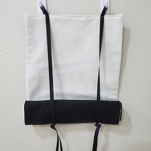 May include: A white and black yoga mat with black straps hanging from two white hooks on a wall. The mat is rolled up and the straps are tied together.