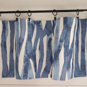 May include: Blue and white patterned valance with a modern abstract design. The valance is made of a soft, textured fabric and hangs from a black metal rod.