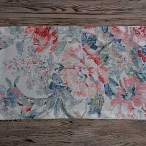 May include: A white table runner with a floral pattern featuring pink, blue, and green flowers. The runner has a vintage, faded look.