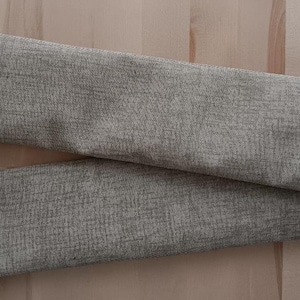 May include: Two pieces of beige fabric with a textured surface. The fabric is folded in half and the ends are overlapping.