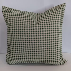 May include: Square decorative pillow with a green and beige gingham pattern. The pillow has a soft, textured appearance and a classic, country-style design. The pillow is a square shape.