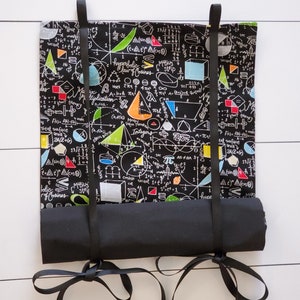 May include: A black fabric roll-up pouch with black ribbon ties. The pouch is printed with white mathematical equations and formulas, including geometric shapes, and the words "hyperbolic law of cosines", "Moebius strip", and "integers".