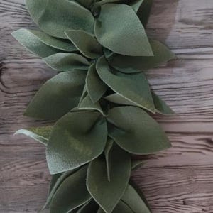 May include: A garland of felt leaves in shades of green, arranged in a cascading pattern. The leaves are made of felt and have a soft, textured appearance.