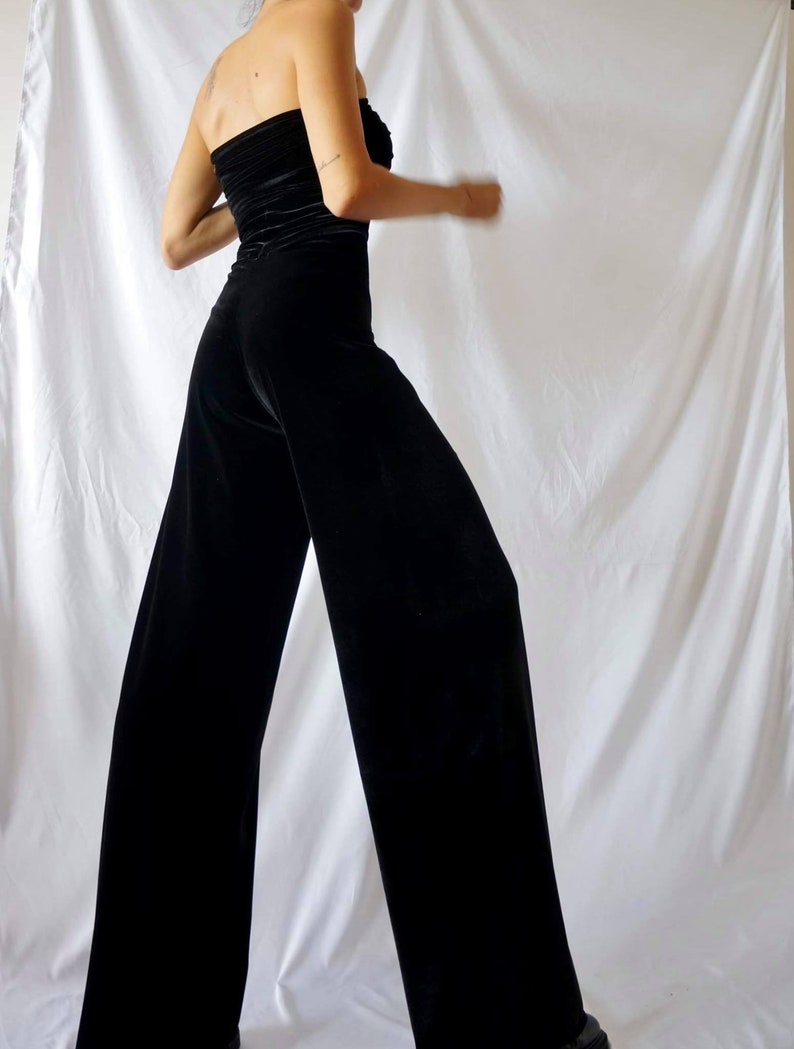 May include: A black velvet strapless jumpsuit with wide legs. The jumpsuit is fitted at the waist and has a relaxed fit in the legs.