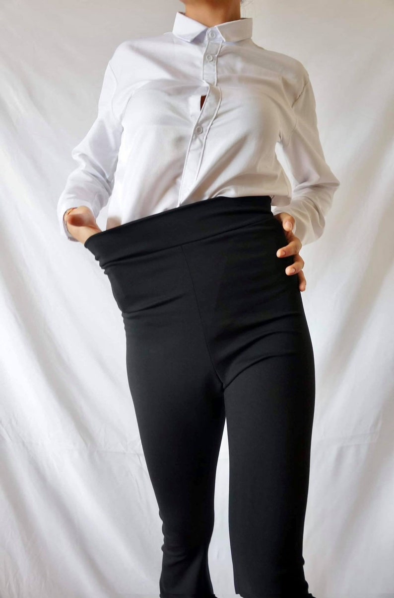 Puede incluir: Una camisa blanca abotonada con un pantal&oacute;n negro de cintura alta.