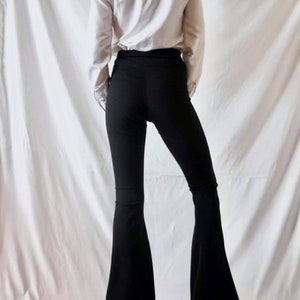 Puede incluir: Una persona con una camisa blanca de manga larga y pantalones negros acampanados.