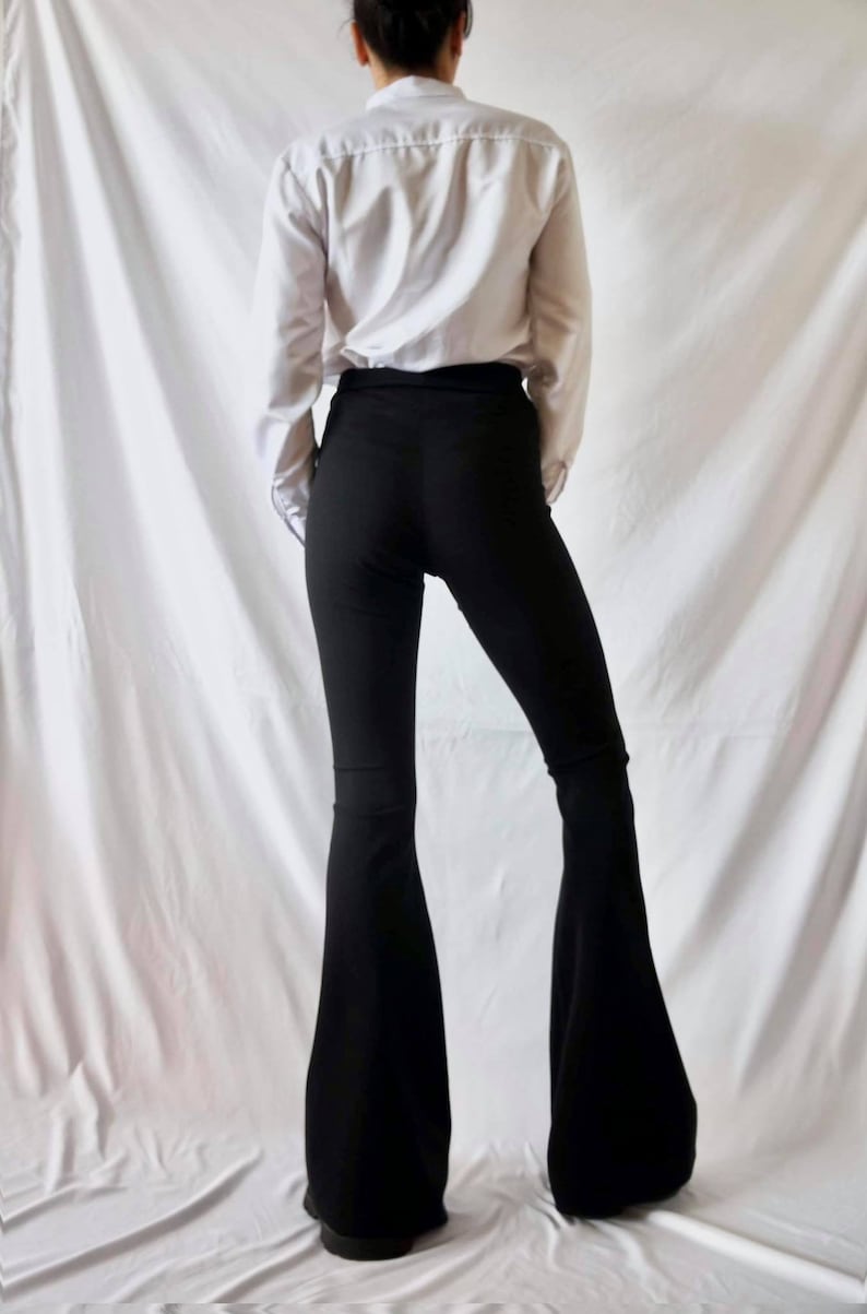 Puede incluir: Una persona con una camisa blanca de manga larga y pantalones negros acampanados.