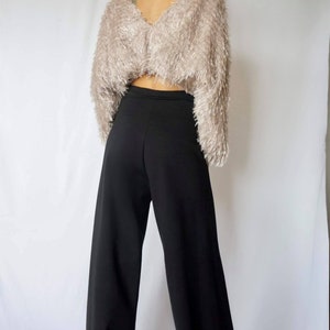 May include: A cropped, long-sleeved, fuzzy, light brown sweater paired with high-waisted, wide-leg black pants. The outfit is shown from the back against a white background. The sweater has a V-neck.