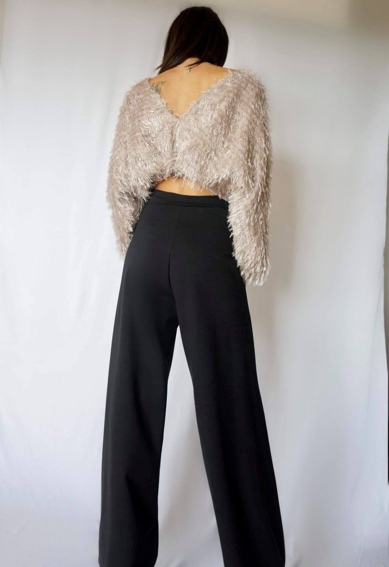 May include: A cropped, long-sleeved, fuzzy, light brown sweater paired with high-waisted, wide-leg black pants. The outfit is shown from the back against a white background. The sweater has a V-neck.