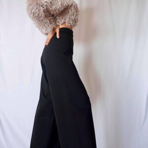 May include: A cropped, fluffy, light brown top paired with high-waisted, wide-leg black pants. The top has a textured, fringed appearance. The pants are a solid, dark black color, creating a contrasting outfit.