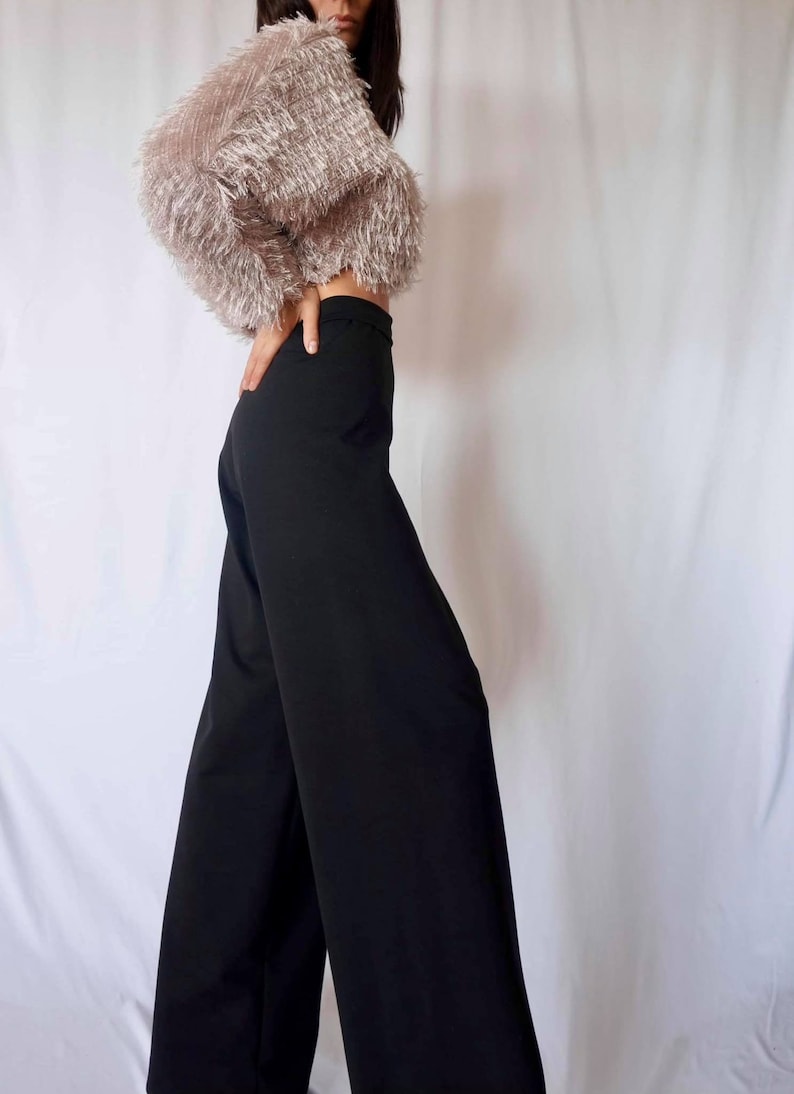 May include: A cropped, fluffy, light brown top paired with high-waisted, wide-leg black pants. The top has a textured, fringed appearance. The pants are a solid, dark black color, creating a contrasting outfit.