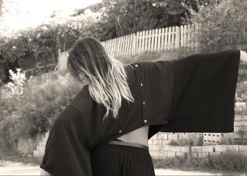 May include: A black, oversized, cropped jacket with a long, flowing sleeve. The jacket is made of a soft, lightweight fabric and has a relaxed fit.