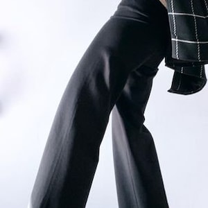 May include: Black wide-leg pants paired with a white top and a black and white plaid blazer. The pants have a high waist and a flowing silhouette. The blazer is draped over the shoulders, adding a touch of sophistication to the outfit.