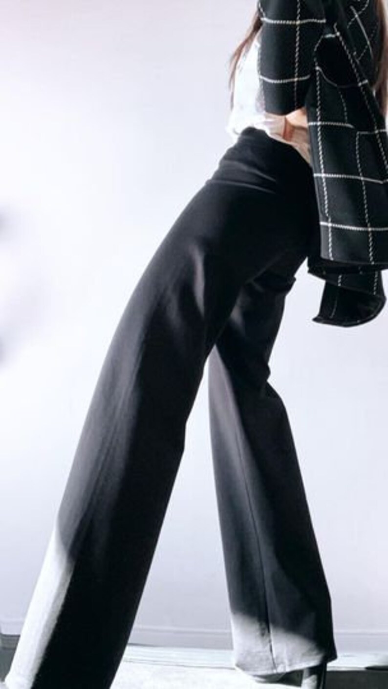 May include: Black wide-leg pants paired with a white top and a black and white plaid blazer. The pants have a high waist and a flowing silhouette. The blazer is draped over the shoulders, adding a touch of sophistication to the outfit.
