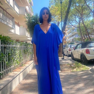 Puede incluir: Un vestido largo azul vibrante con cuello en V y mangas fluidas. El vestido est&aacute; hecho de una tela ligera y se usa con sandalias doradas. Perfecto para un d&iacute;a de verano.