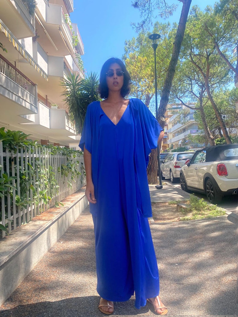Puede incluir: Un vestido largo azul vibrante con cuello en V y mangas fluidas. El vestido est&aacute; hecho de una tela ligera y se usa con sandalias doradas. Perfecto para un d&iacute;a de verano.