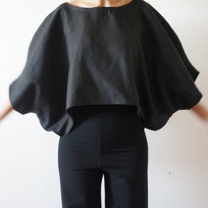 Puede incluir: Una blusa de lino negra con una silueta amplia y fluida. La blusa tiene un corte holgado y una longitud recortada.