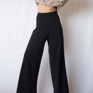 May include: Black wide-leg pants with a high waist. The pants are made of a smooth, solid black fabric. The pants are shown against a white background.