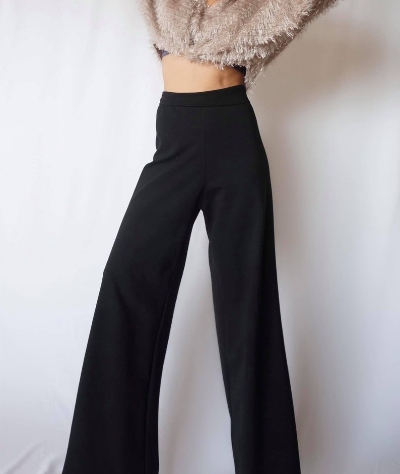 May include: Black wide-leg pants with a high waist. The pants are made of a smooth, solid black fabric. The pants are shown against a white background.