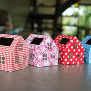May include: Four miniature paper houses with different patterned designs. The houses are red, pink, blue, and white with gingham, floral, polka dot, and star patterns.