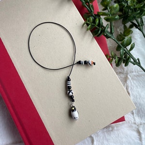 May include: A black and white penguin charm bookmark with black and white beads and a black string.