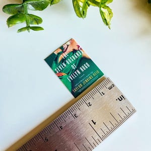 Puede incluir: Un libro de bolsillo titulado "Los Siete Maridos de Evelyn Hugo" de Taylor Jenkins Reid. La portada muestra a una mujer con un vestido verde y una flor roja en el pelo.