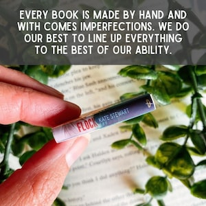 May include: A miniature book spine titled Flock by Kate Stewart with a purple and white gradient cover. The text reads: EVERY BOOK IS MADE BY HAND AND WITH COMES IMPERFECTIONS. WE DO OUR BEST TO LINE UP EVERYTHING TO THE BEST OF OUR ABILITY.