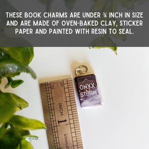 May include: A miniature book charm titled Onyx Storm by Rebecca Yarros, crafted from oven-baked clay and sticker paper with a resin seal. The charm features a gold jump ring and is shown next to a metal ruler, measuring under 3/4 inch in size.