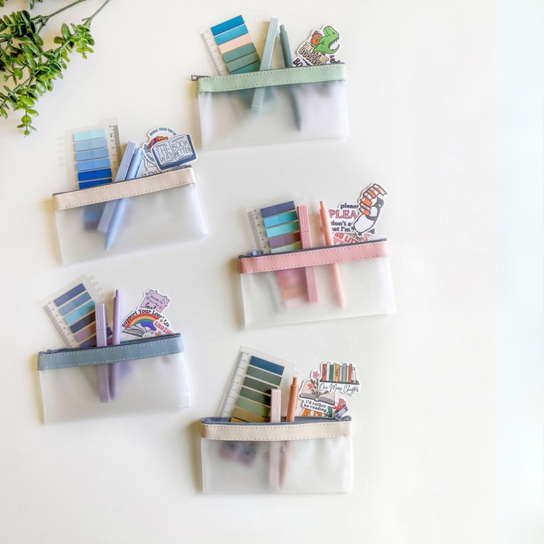 May include: Four clear zippered pouches with different colored trim, each filled with colorful stationery, including pens, highlighters, and sticky notes. The pouches are on a white surface.
