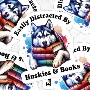 May include: A sticker featuring a cartoon husky with blue eyes, resting its head on a stack of colorful books. The sticker has the text "Easily Distracted By Huskies & Books" and watercolor-style blue and pink splatter paint.