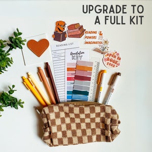 May include: A brown and beige checkered pencil case with a variety of colorful pens, pencils, and markers inside. The case is surrounded by stickers with book-themed designs, including "Reading Powers", "Imagination", and "Open to Book Recs".