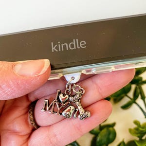 Puede incluir: Un charm plateado con las palabras "I love my" y un charm de hueso de perro unido a una funda de Kindle de plástico blanco. La funda de Kindle tiene la palabra "kindle" impresa.