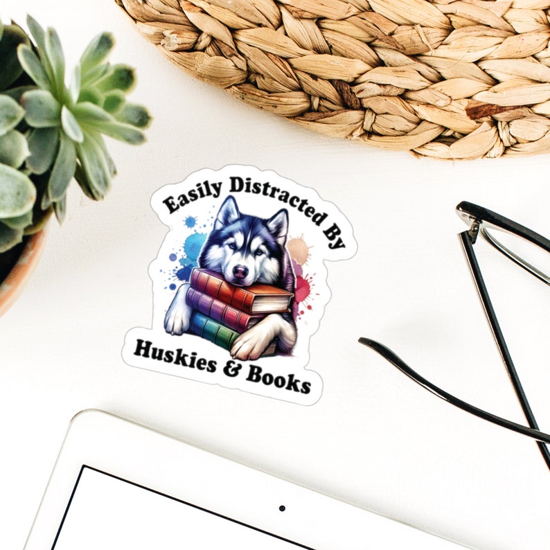 May include: A white sticker with a black and white husky dog holding a stack of colorful books. The sticker says "Easily Distracted By Huskies & Books".