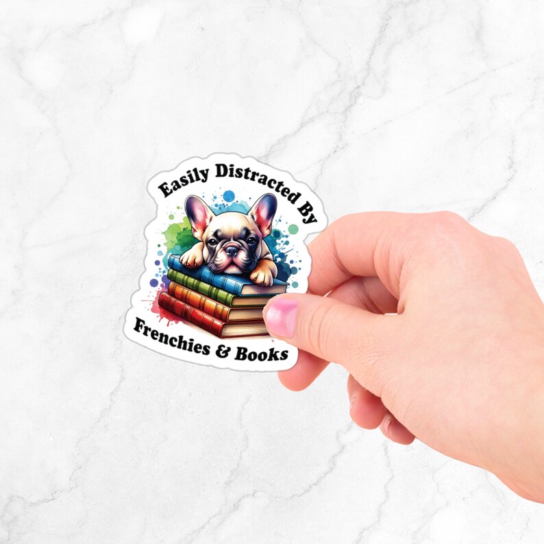 May include: A sticker featuring a cartoon French bulldog puppy lying on a stack of books. The sticker has the text "Easily Distracted By Frenchies & Books" around the image.