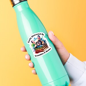 May include: A teal water bottle with a sticker that says "Easily Distracted By Frenchies & Books". The sticker features a cartoon French bulldog lying on a stack of colourful books.