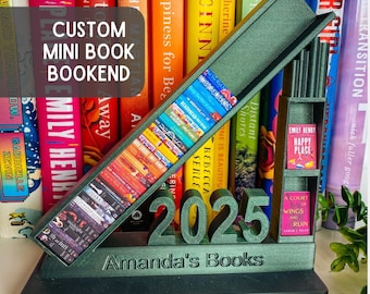 May include: A custom mini book bookend in a dark green color. The bookend features a slanted shelf filled with miniature book replicas, the year "2025", and the text "Amanda's Books". The text "CUSTOM MINI BOOK BOOKEND" is also visible.