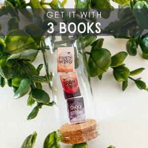 May include: A glass bottle with a cork stopper contains three miniature books. The books are titled "Fourth Wing", "Iron Flame", and "Onyx Storm". The text "Get it with 3 books" is displayed above the bottle.