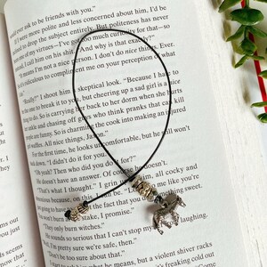 May include: A black leather bookmark with silver and gold beads and a silver zebra charm. The bookmark is on a page of a book with text about friendship and politeness.