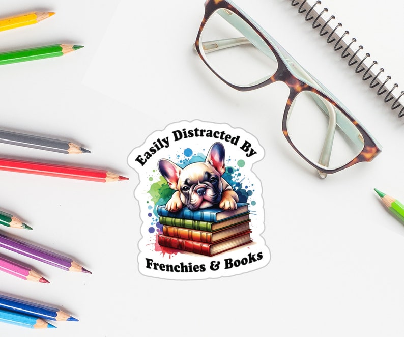 May include: A white French bulldog puppy with brown ears is lying on a stack of colourful books. The text "Easily Distracted By Frenchies & Books" is written in black on a white background.