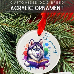 May include: A white round acrylic Christmas ornament with a colorful watercolor background. A cartoon husky dog wearing glasses is reading a book. The dog's name, "Sammy", is written in cursive on the ornament.