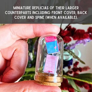 May include: A miniature replica of a book in a glass jar with a cork stopper. The book is pink and blue with white text. The jar is clear glass and the cork is brown.