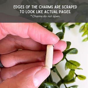 May include: A small book-shaped charm with light beige, textured edges that are scraped to resemble individual pages. The charm is solid and does not open. Text on the image reads: EDGES OF THE CHARMS ARE SCRAPED TO LOOK LIKE ACTUAL PAGES. *Charms do not open.