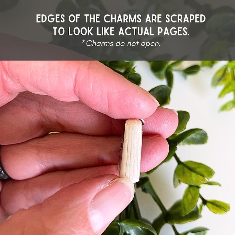 May include: A small book-shaped charm with light beige, textured edges that are scraped to resemble individual pages. The charm is solid and does not open. Text on the image reads: EDGES OF THE CHARMS ARE SCRAPED TO LOOK LIKE ACTUAL PAGES. *Charms do not open.