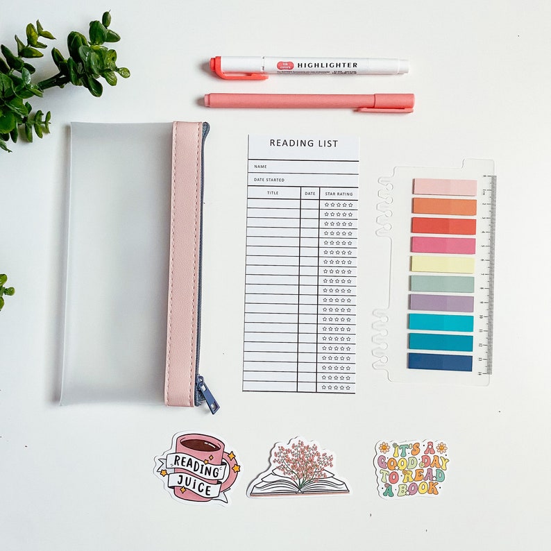May include: A flat lay of reading-themed stationery items on a white surface. The items include a pink pencil case, two pink highlighters, a reading list tracker with a star rating system, a ruler, colorful sticky notes, and three stickers. The stickers are: a cup of coffee with the words 'Reading Juice', a book with flowers, and a colorful sticker with the text 'It's a good day to read a book'.